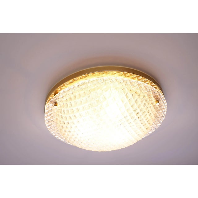 This flush mount was manufactured by Fischer Leuchten in Germany. The light has a brass finish and a textured glass shade....