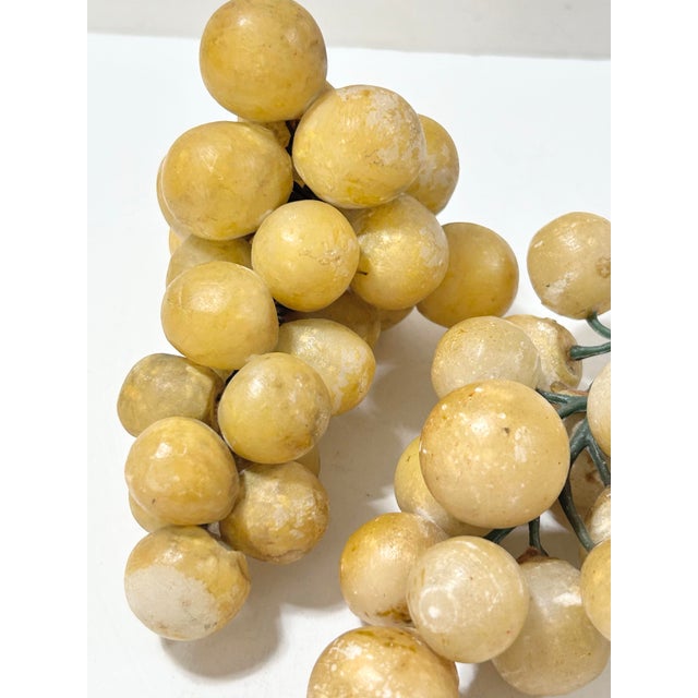Pair of decorative stone grape clusters in warm yellow and cream tones with green stems. Display together in a shallow...