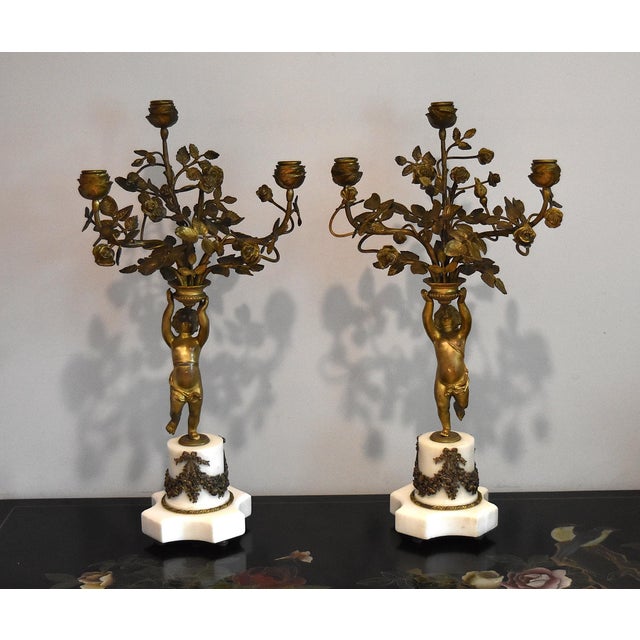 A wonderful complimenting pair of gilt bronze marble based Louis XVI style cherub candleabras with bronze mounts. This...