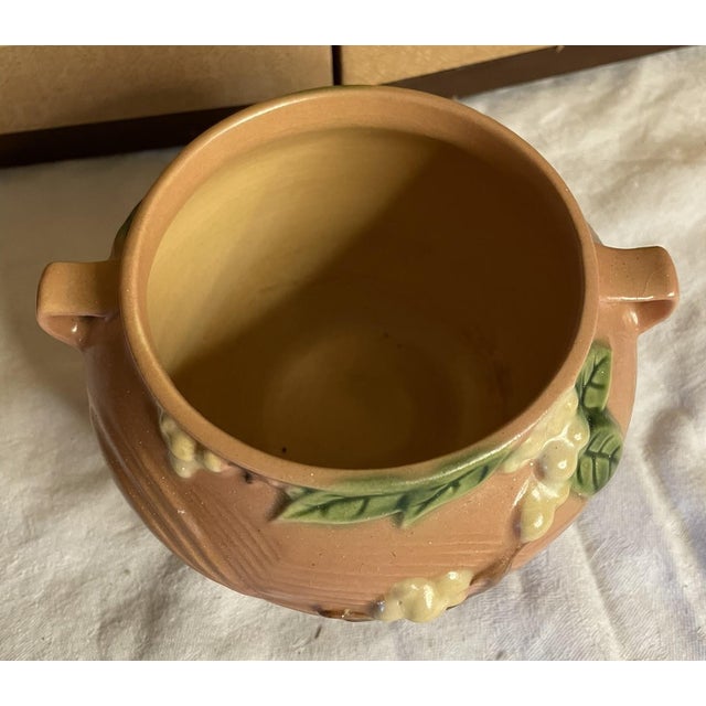 This charming 4-inch Roseville Pottery jardinière features a delicate pink hue and a classic double-handled design....