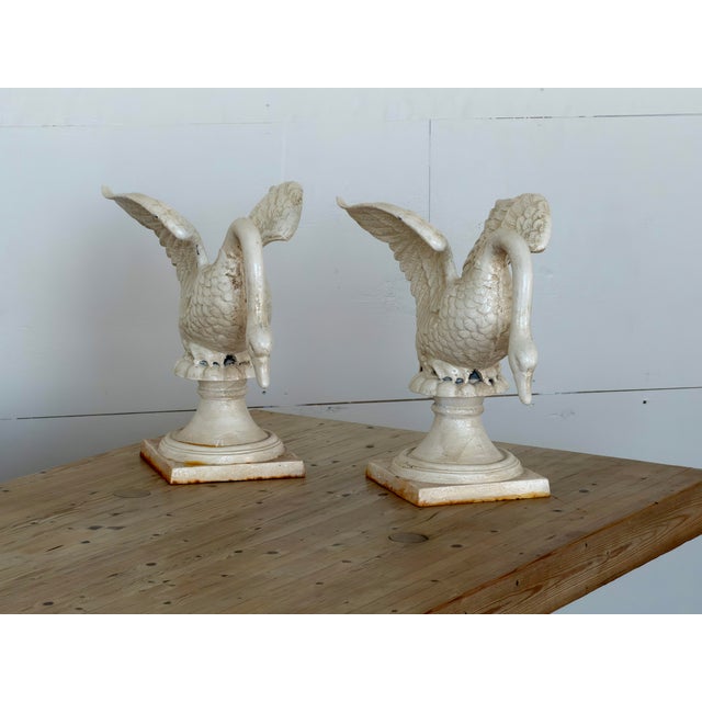This cast iron swan figures is finished in an antique white paint and mounted on stepped socle bases with square plinths....