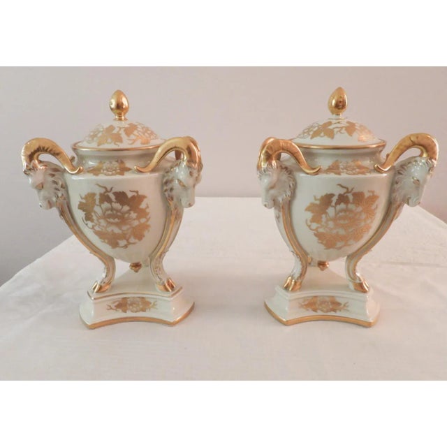 This marvelous pair of antique covered urns are created in gorgeous white porcelain with gold gilt design by the Art...