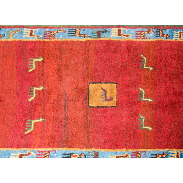 A beautiful mid-20th century Persian Gabbeh rug with a fabulous abrash crimson field covered in goats and human figures,...
