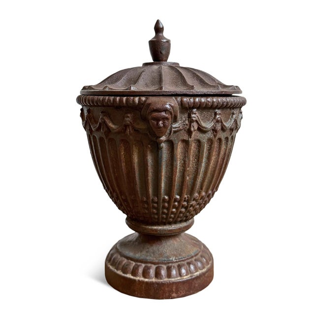 Vintage old world style cast iron lidded urn featuring a beautifully fluted body with garland motifs, decorative mask...