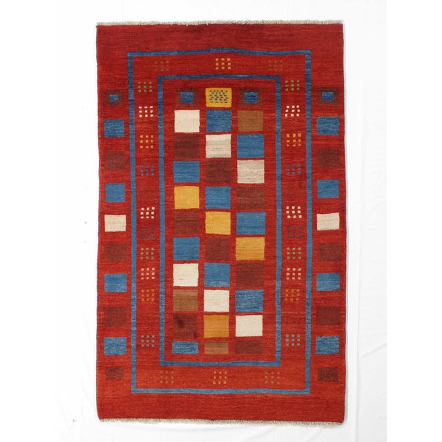 Vintage Hand-knotted Persian Lori Gabbeh rug featuring a bold geometric patchwork design set within a rich red field. The...
