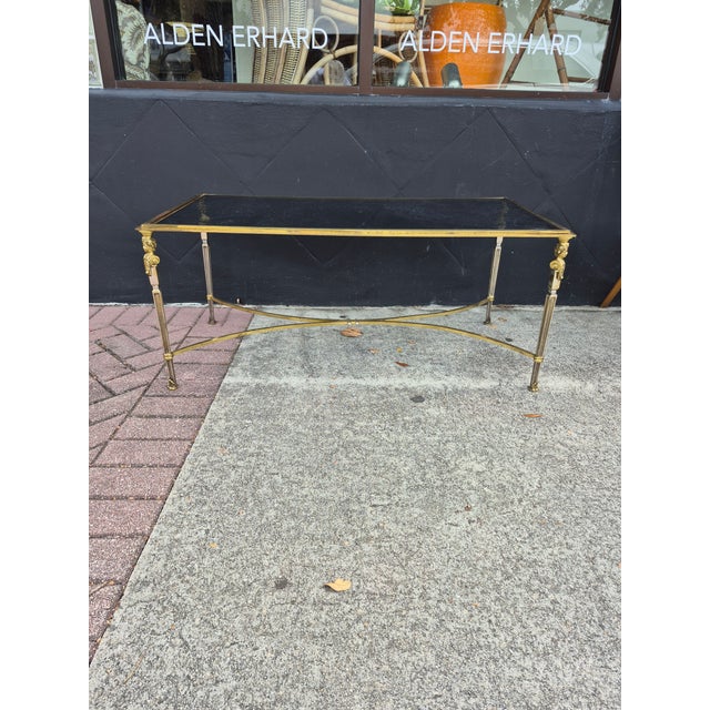 Chic vintage coffee table crafted in brass and steel in Neoclassical forn with figural highlights under a glass top....