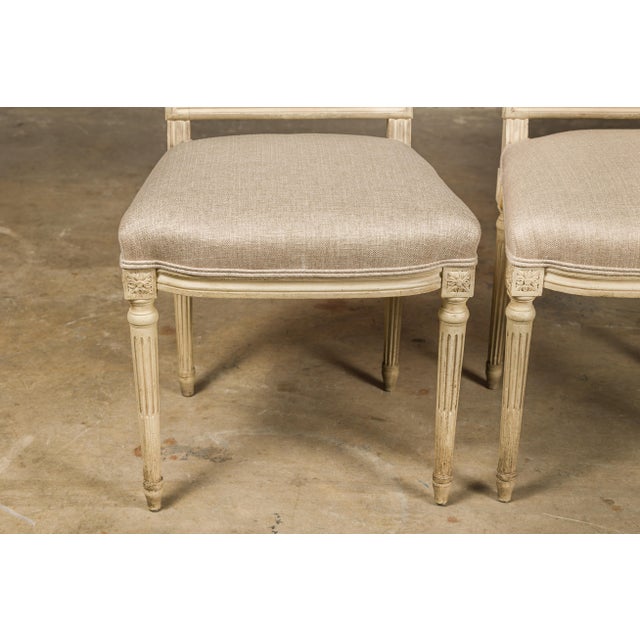 A pair of French Louis XVI style painted side chairs from circa 1920 with rectangular backs, fluted legs, carved rosettes...