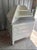 A crisp white display cabinet topped with a heavy slab of real gray-and-white marble. A tiered, angled shelf unit rises...