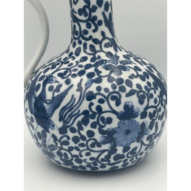 A beautifully hand painted blue and white chinoiserie porcelain ewer featuring a graceful curved handle, bulbous body, and...