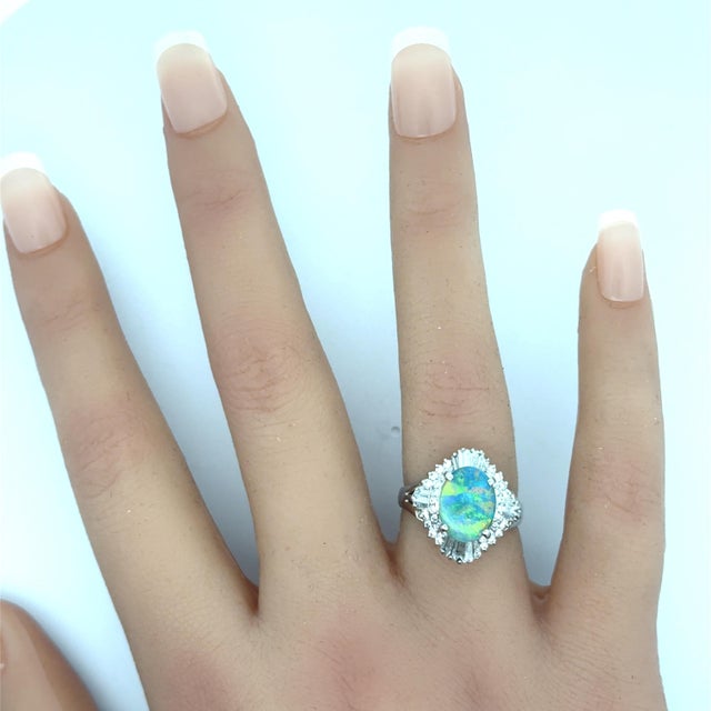 A striking ring featuring a 1.75-carat oval black opal. The opal displays a vibrant rainbow of colors. Surrounding the...