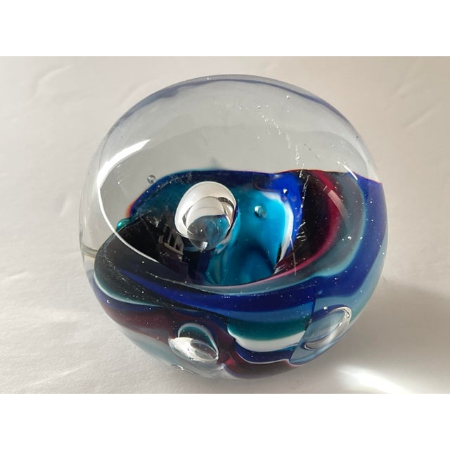 Hand blown glass paperweight with interior ocean wave with hues of turquoise, deep indigo, sky blue, cadet blue and...