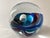 Hand blown glass paperweight with interior ocean wave with hues of turquoise, deep indigo, sky blue, cadet blue and...