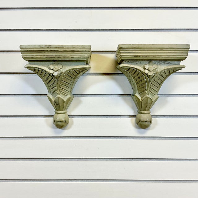 This pair of hand-carved wood wall-mounted shelves feature Palm Fronds at the base with a daisy-like flower. They are both...