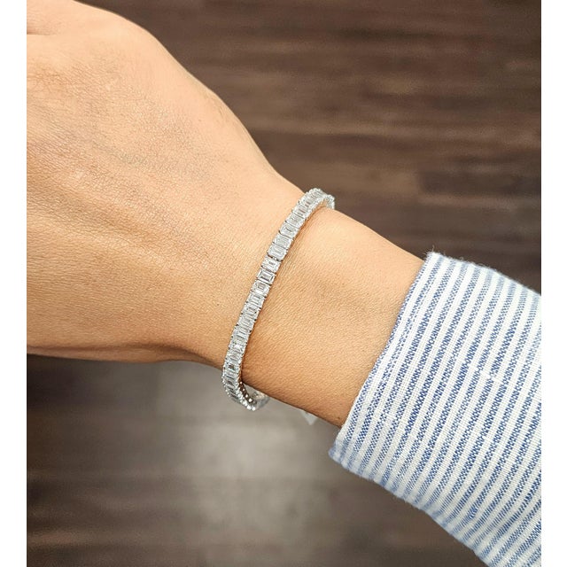 This elegant tennis bracelet exudes modern sophistication. Featuring a continuous line of 62 natural emerald-cut white...