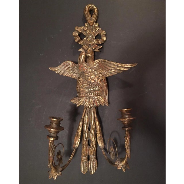 This wood carved and gold gilded antique sconce features a majestic eagle with spread wings beneath a tied bow. The candle...