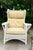 A white finish wicker rattan wingback chair with yellow removable cushions and a magazine pocket holder on the side of the...