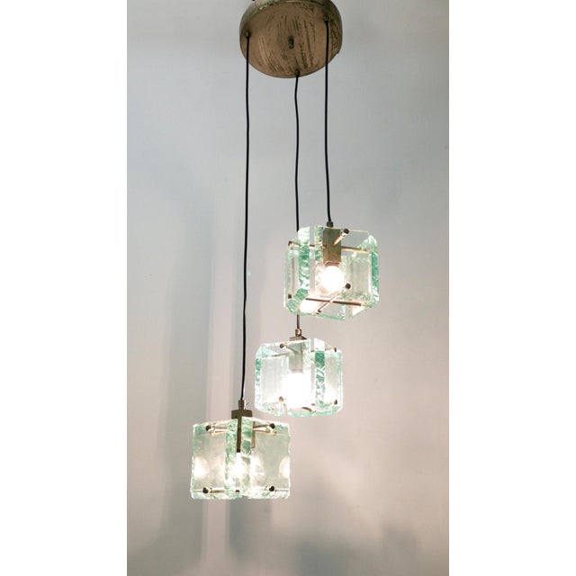 Made in Italy, 1960s. This pendant features thick Nile green hammered glass lampshades and varnished metal parts. The...