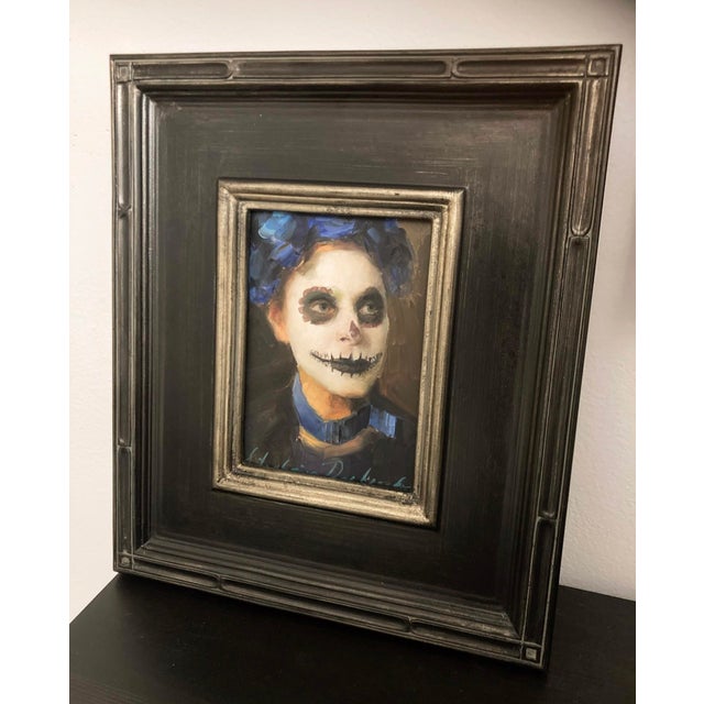 This oil on panel work captures a woman adorned for the Day of the Dead, her face painted with traditional skull motifs...