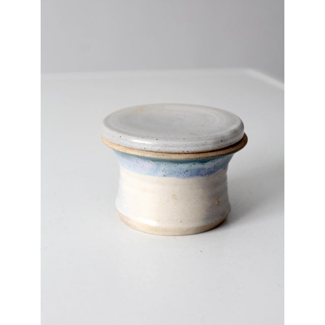 This vintage studio pottery butter keeper features a softly speckled cream glaze accented by bands of pale blue and...