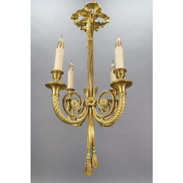 - French Louis XVI style bronze four-light bow, ribbon, and tassel chandelier from the early 20th century. - An elegant...