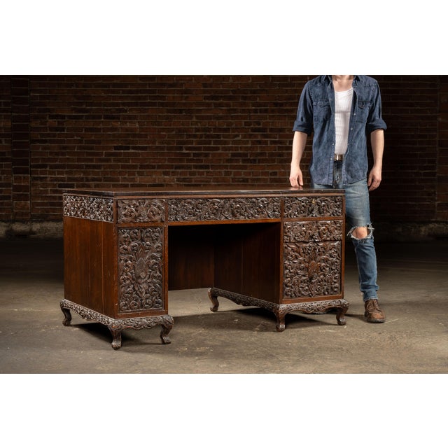 Hand-carved Indonesian hardwood kneehole desk featuring elaborate floral and foliate relief carving across the drawer...