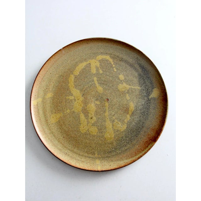 A vintage handmade studio pottery plate with a low, open form and a softly irregular rim that reflects its handcrafted...