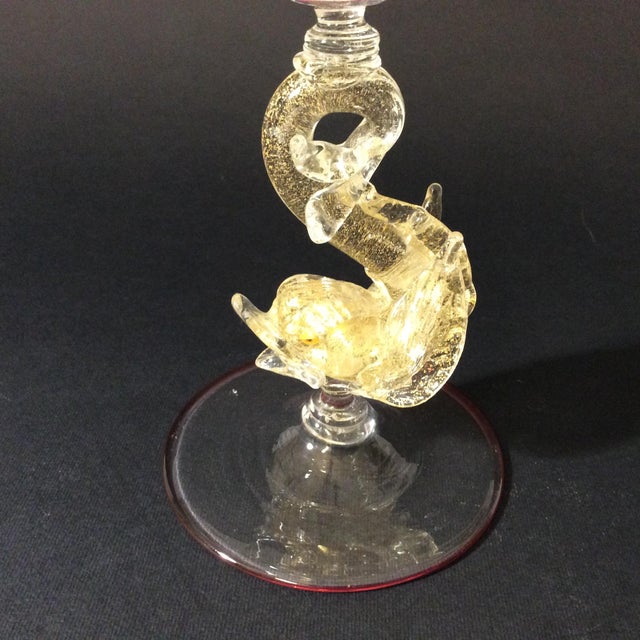 A thin, blown glass cup, finished with red edges and a dolphin-shaped stem with gold leaf inclusions. The design is by...
