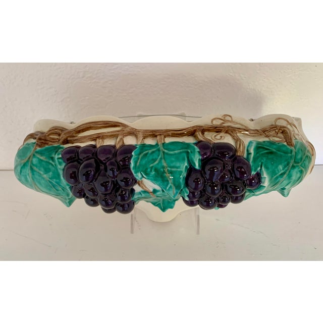 A vintage, ceramic, majolica wall pocket shaped like a vase overrunning with lush vines and blue grapes. This would be a...