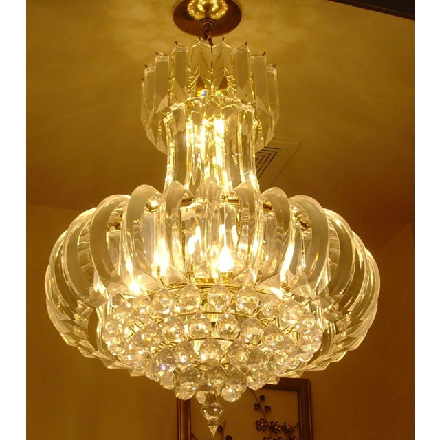 Featured is a six-tiered lucite chandelier with a gold-tone metal base. Measuring approximately 28 inches tall by 20...