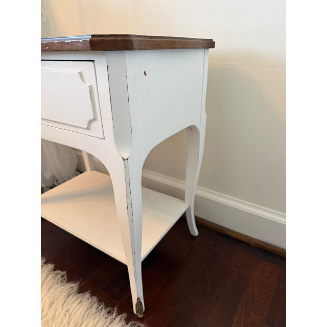 Sweet side table with a wooden top over a distressed white painted bottom. Table features a single drawer with brass pull...