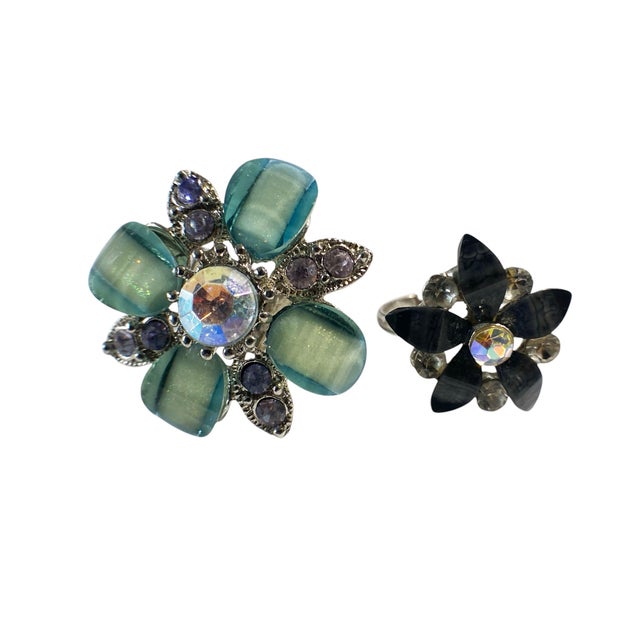 This set includes two beautifully crafted vintage rings, each with a unique flower shape and diamond accents. The first...