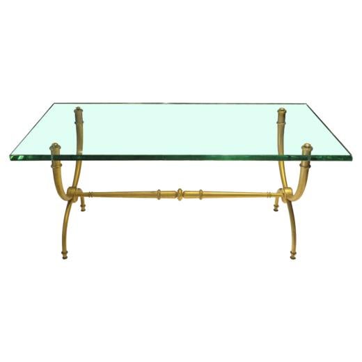 French Art Deco coffee table with glass top. The metal legs have a gold finish and feature small decorative accents.