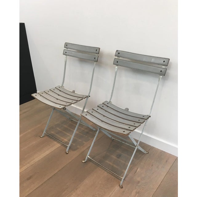 This pair of folding chairs is made of white lacquered metal with a grey leather seat and back. These are comfortable and...