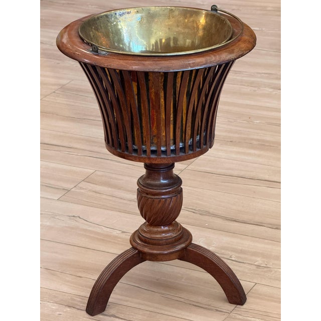 An early 19th C. English flared mahogany bucket made of slender curved slats beneath a molded rim, holding a removable...