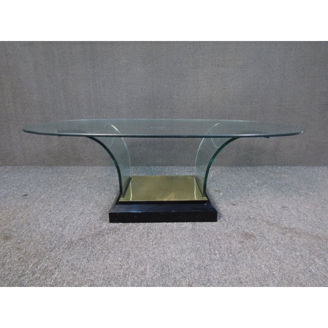 With an oval glass top and glass supports curving into a brass base, this vintage coffee table is sure to impress.