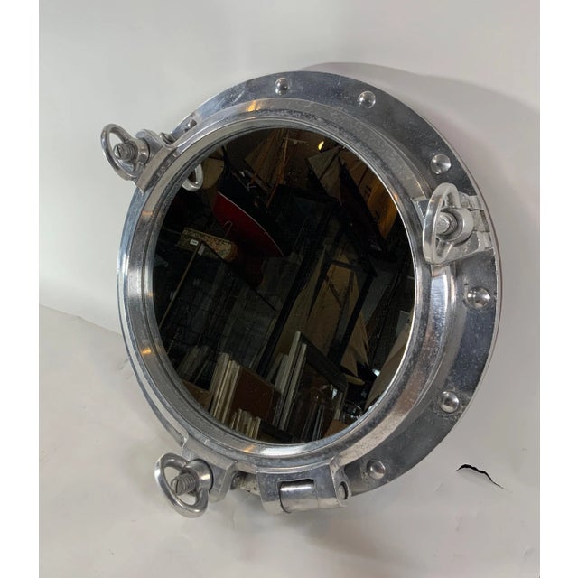 Massive authentic polished aluminum ship's porthole fitted with a glass mirror. Door is hinged and fitted with three...