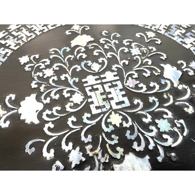 A vintage Chinese low table crafted in black lacquer and richly inlaid with mother-of-pearl, featuring an intricate...