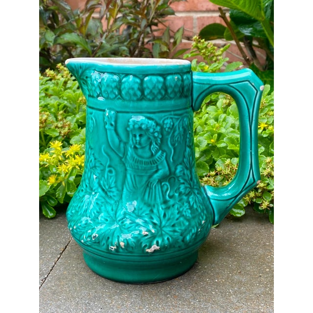 Gorgeous turquoise glazed Majolica pitcher featuring relief images of a boy playing an instrument on one side and a girl...