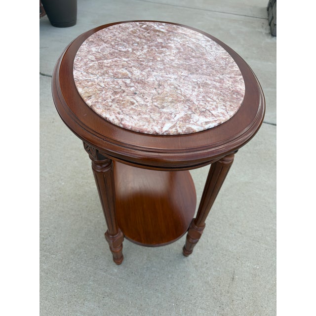 Elegant vintage oval side table featuring a beautiful pink-toned marble top set over a richly finished wood base. Designed...