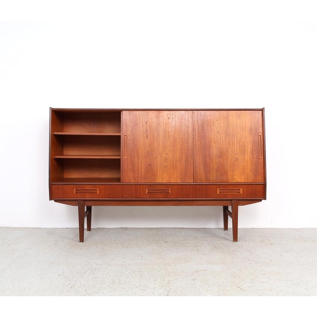 Danish design highboard from the 1960s, crafted in teak veneer. The unit features three sliding doors and three spacious...