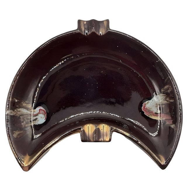 Mid-century brown crescent-shaped ashtray with gold and multicolored accents. The rich brown glaze enhances its sculptural...