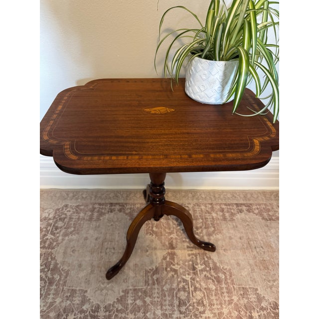 An elegant antique tilt-top table, finely crafted with rich wood grain, graceful proportions, and a striking shell-form...