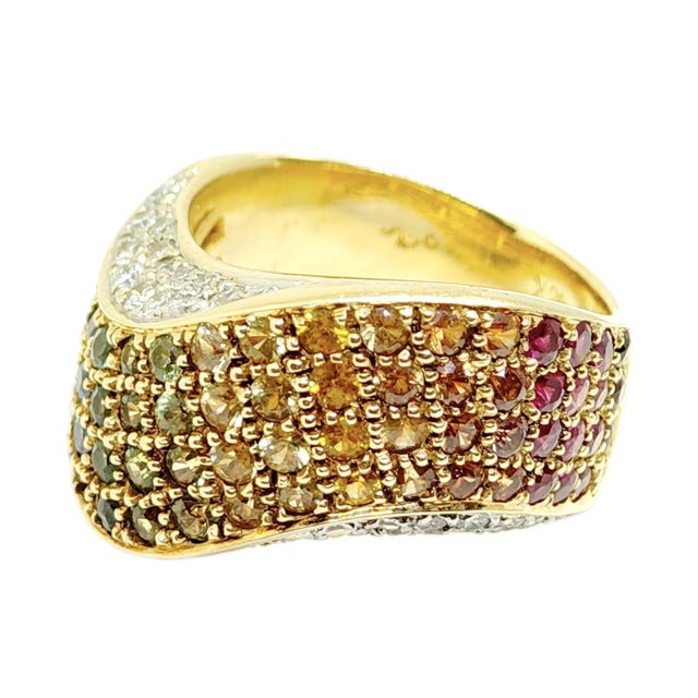 Crafted in 18k yellow gold, this wide wavy band design features a vibrant array of round-cut multi color sapphires...