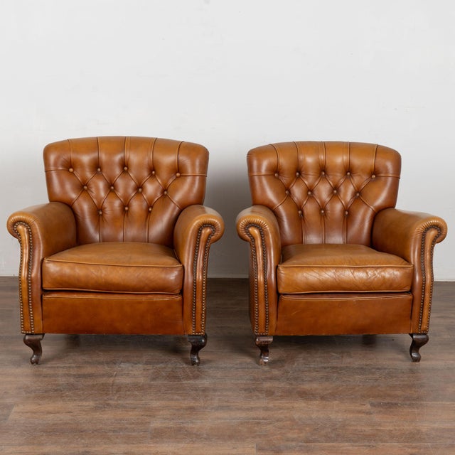 Pair of leather club chairs from Spain. Upholstered in vintage brown leather, the chairs feature tufted button backs, and...