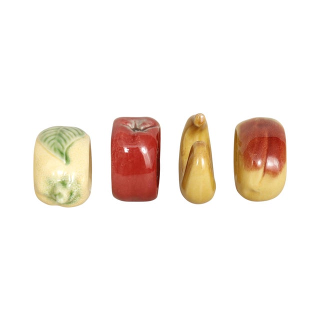 A set of four ceramic fruit themed napkin rings. Individual rings are shaped like red and green apples, a lemon, and a...