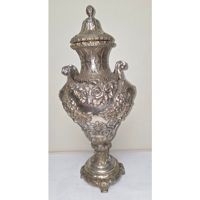 This decorative bronze urn features a silver-colored finish with touches of rustic gold that give it a unique, aged...