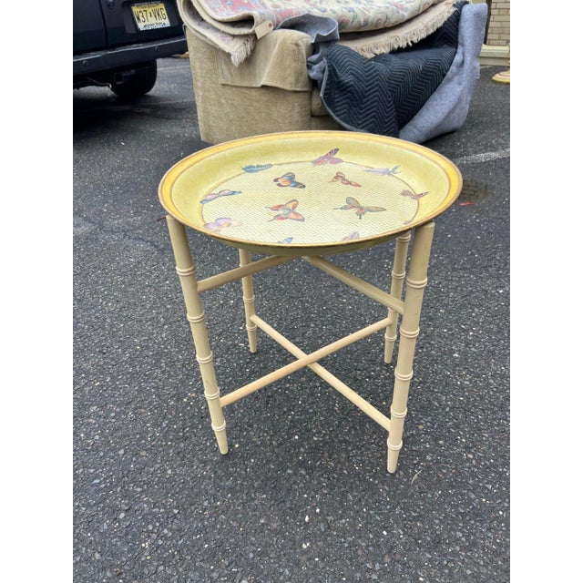 A charming round folding tray table featuring a removable top adorned with colorful butterfly motifs set against a warm...