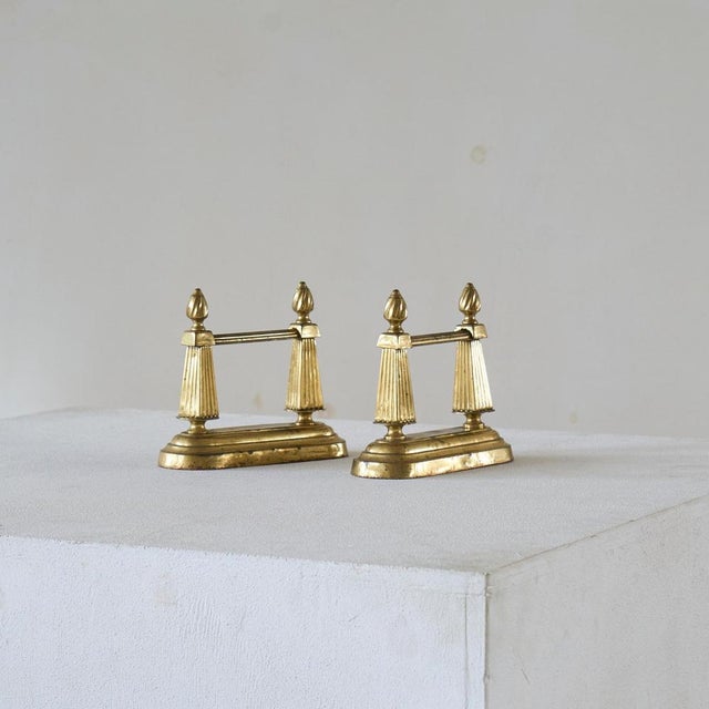 Pair of Neoclassical Andirons in Patinated Brass. Europe, late 19th century. A wonderful pair of neoclassical andirons or...