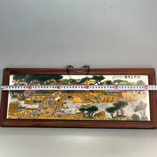 A vibrant Chinese porcelain plaque mounted in a dark wood frame with a brass hanging loop. The plaque features a detailed,...