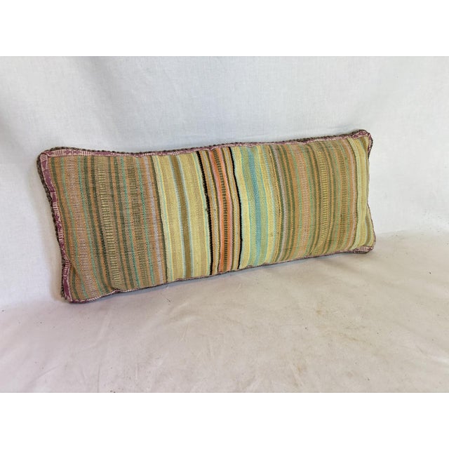 This pillow is made from belts. It has blue, yellow, orange, green, brown pink, purple, brown and black stipes.